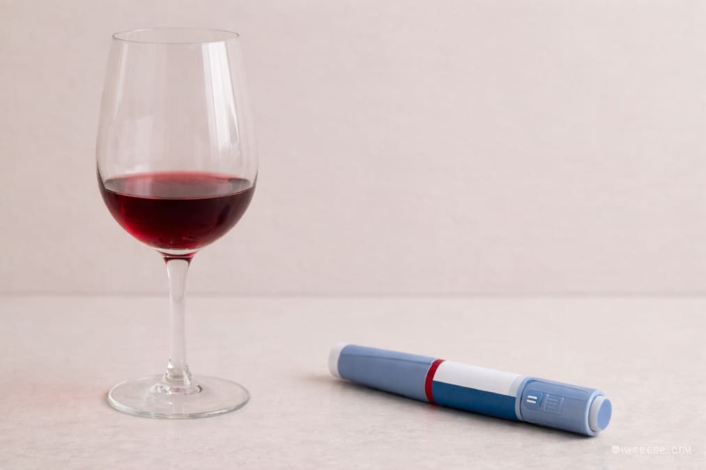 A glass of red wine beside a GLP-1 injection pen, illustrating the relationship between wine and weight-loss medication.