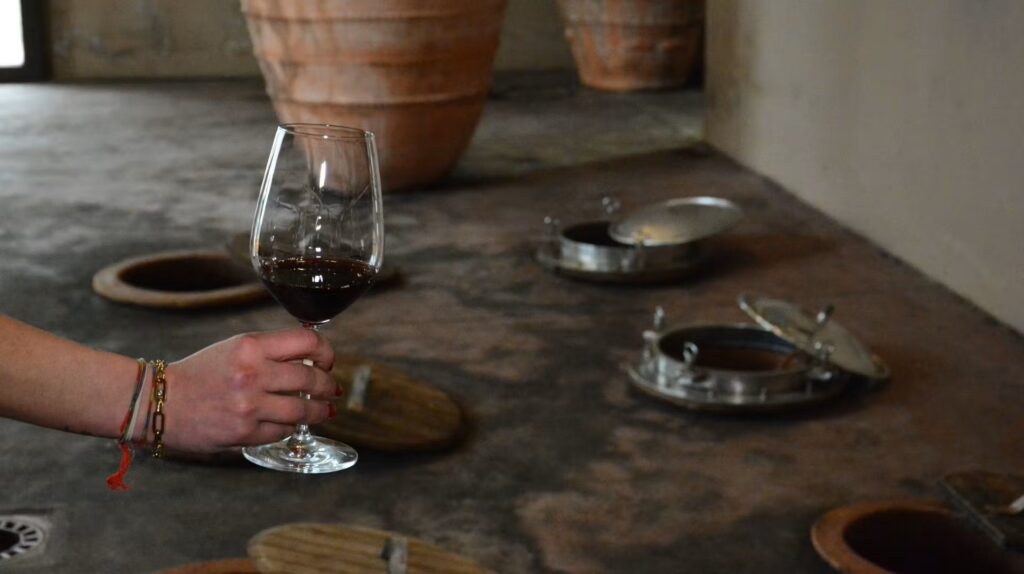 Wine being tasted beside traditional Georgian qvevri buried in the ground, illustrating the ancient method of fermenting and ageing wine in clay vessels.